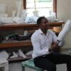 A kenyan prosthetic technician is sitting on a bench and holding a socket he manufactured for a lower limb amputee