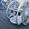 Picture of a wheelchair prototype fully made in alluminium. The wheelchair has no backrest and the rear wheels have smaller wheels placed perpendicularly that allows it to travel sideways