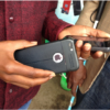 A shop assistant in Kenya holding two smartphones to help a customer with visual impairment perform an operation